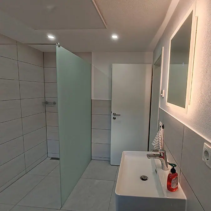 Badezimmer mit moderner Dusche, Waschbecken und Spiegel, ausgestattet mit neutralen Fliesen und einfacher Beleuchtung.