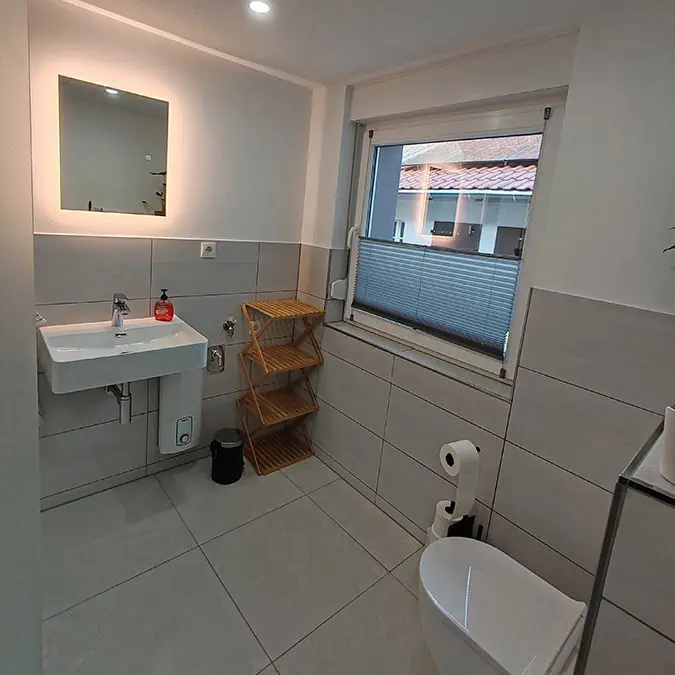 Modernes Badezimmer mit einem weißen Waschbecken, einer Toilette und einem Holzregal in neutralen Farbtönen.