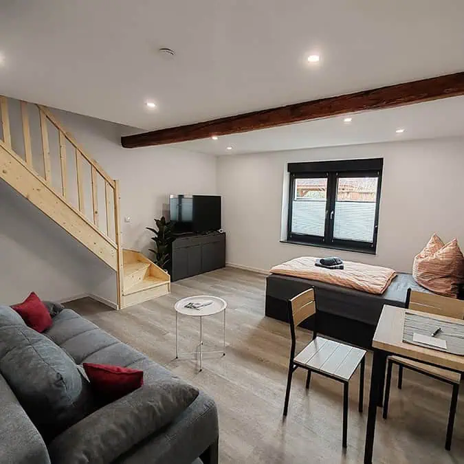 Modernes Wohnzimmer mit einer Treppe, einem Sofa, einem Tisch und Stühlen sowie einem Fernseher und einem Fenster.