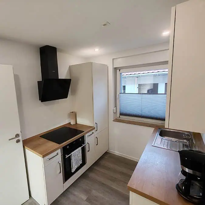 Küche mit Kochfeld, Dunstabzugshaube, Spüle und Holzarbeitsfläche in einem modernen Design.