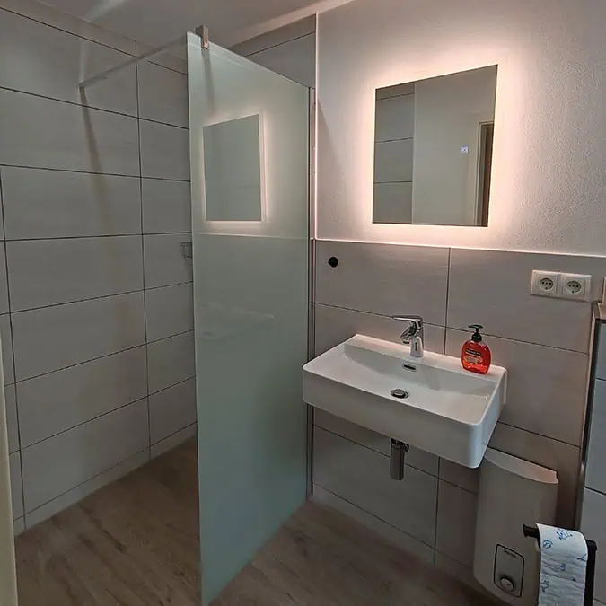Modernes Badezimmer mit einer Glasdusche, einem Waschbecken und einem Spiegel an der Wand.