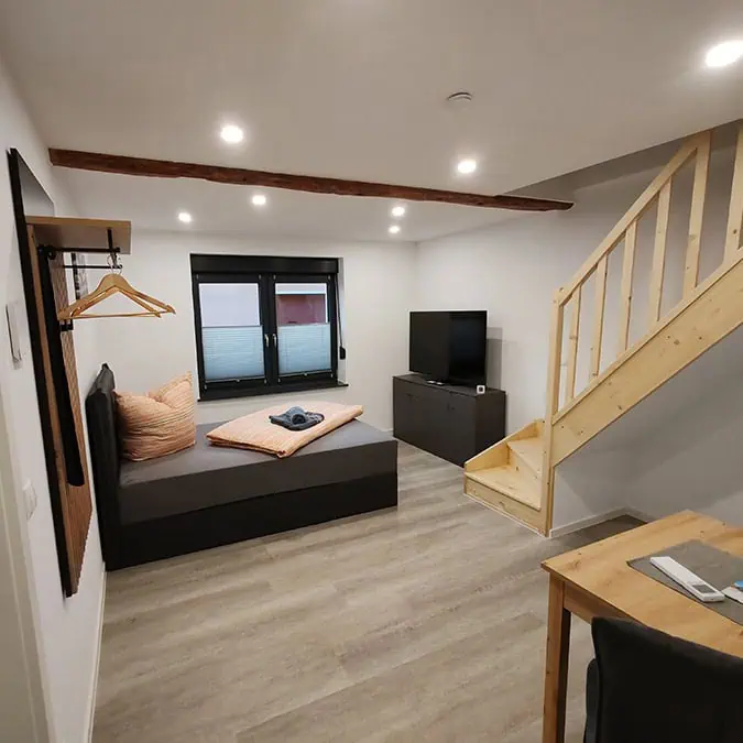 Helles Erdgeschoss-Apartment mit einem Bett, einem Fernseher, einem Tisch und einer Treppe aus Holz.