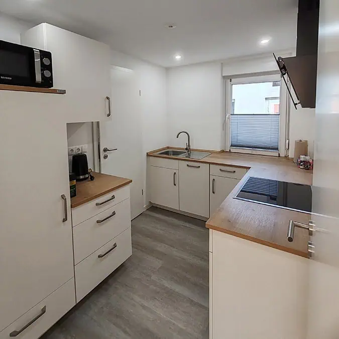 Küche mit weißen Schränken, Holzarbeitsfläche, Spüle und Kochfeld in einem hellen Raum.