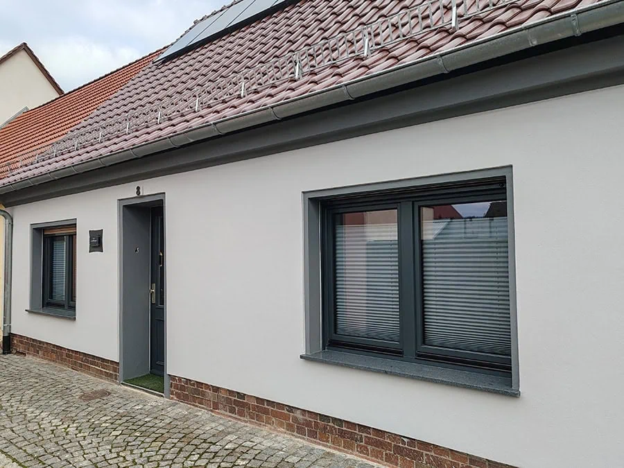 Moderne Fassade eines Wohnhauses mit grauen Fenstern und einem Eingangstür auf der linken Seite.